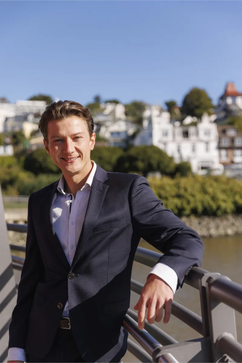 LUV-LEE-Immobilien Tim Reumann Tim Reumann stehend an der Elbe mit dem Süllberg als Hintergrund