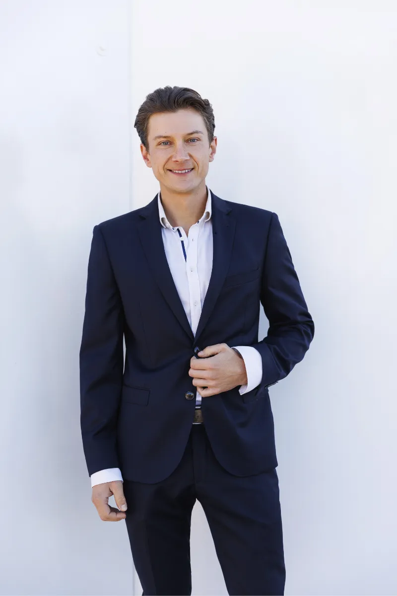 Tim Reumann Immobilienmakler LuvLee Tim Reumann,Immobilienmakler, steht vor einer hellen Wand